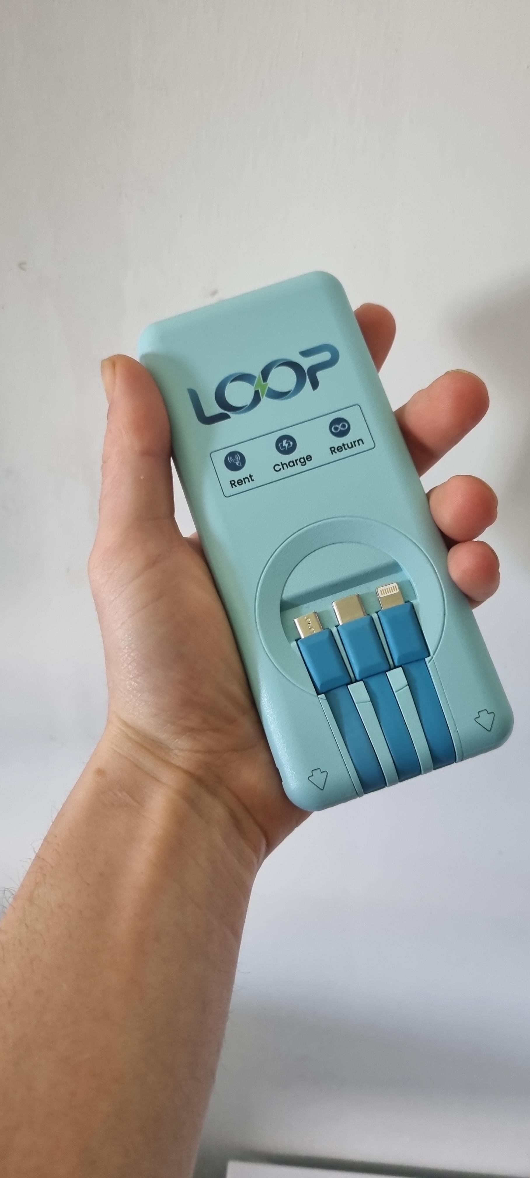 A hand holding a Loop power bank. Three charging cables are built into the top: Lightning, USB-C and USB-A.