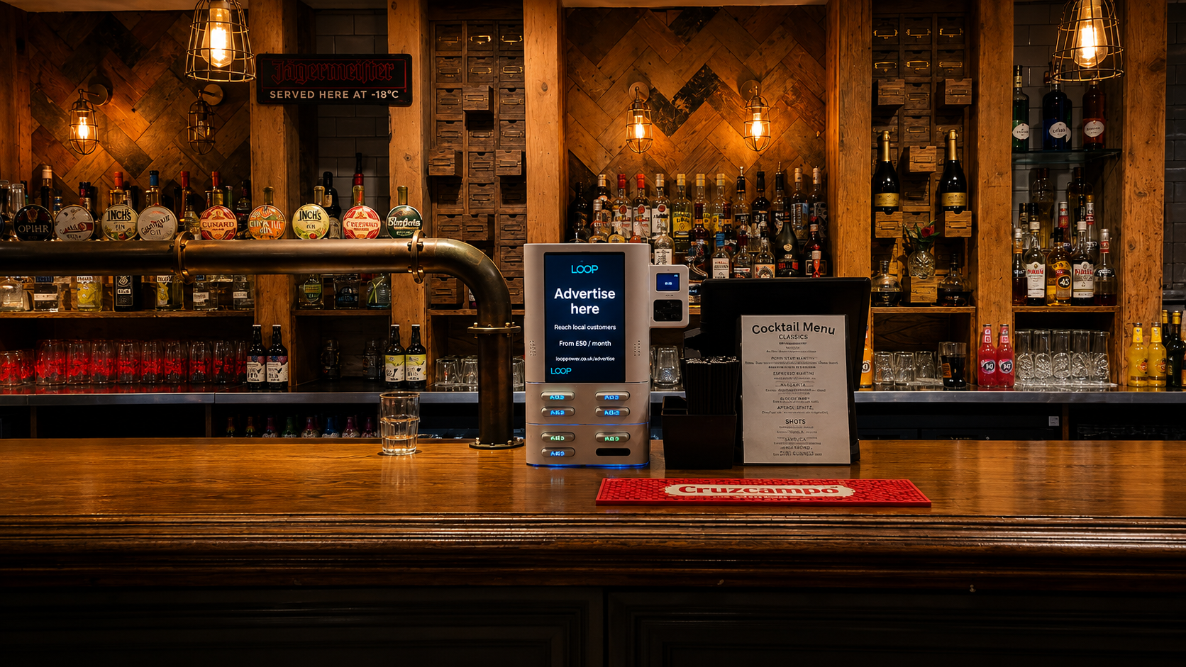 A Loop charging station on a pub bar. The screen reads: Advertise here, reach local customers, from £50 a month.
